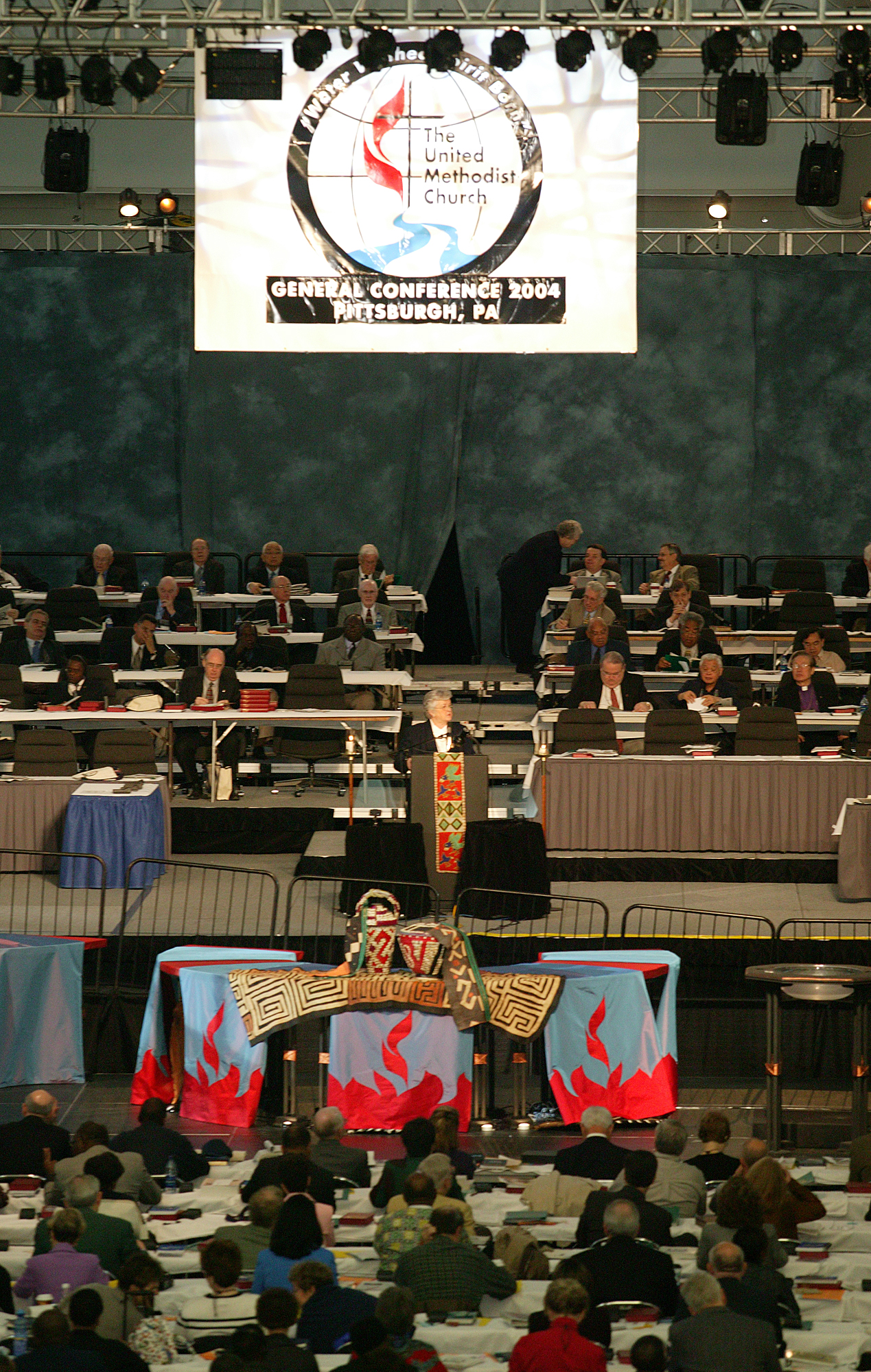 Sandra Kelley Lackore (at podium, center), top staff executive of the United Methodist Church's General Council on Finance and Administration, holds a church offering plate as she discusses the financial state of the church during the denomination's 2004 General Conference in Pittsburgh. A UMNS photo by Rasul Welch.
