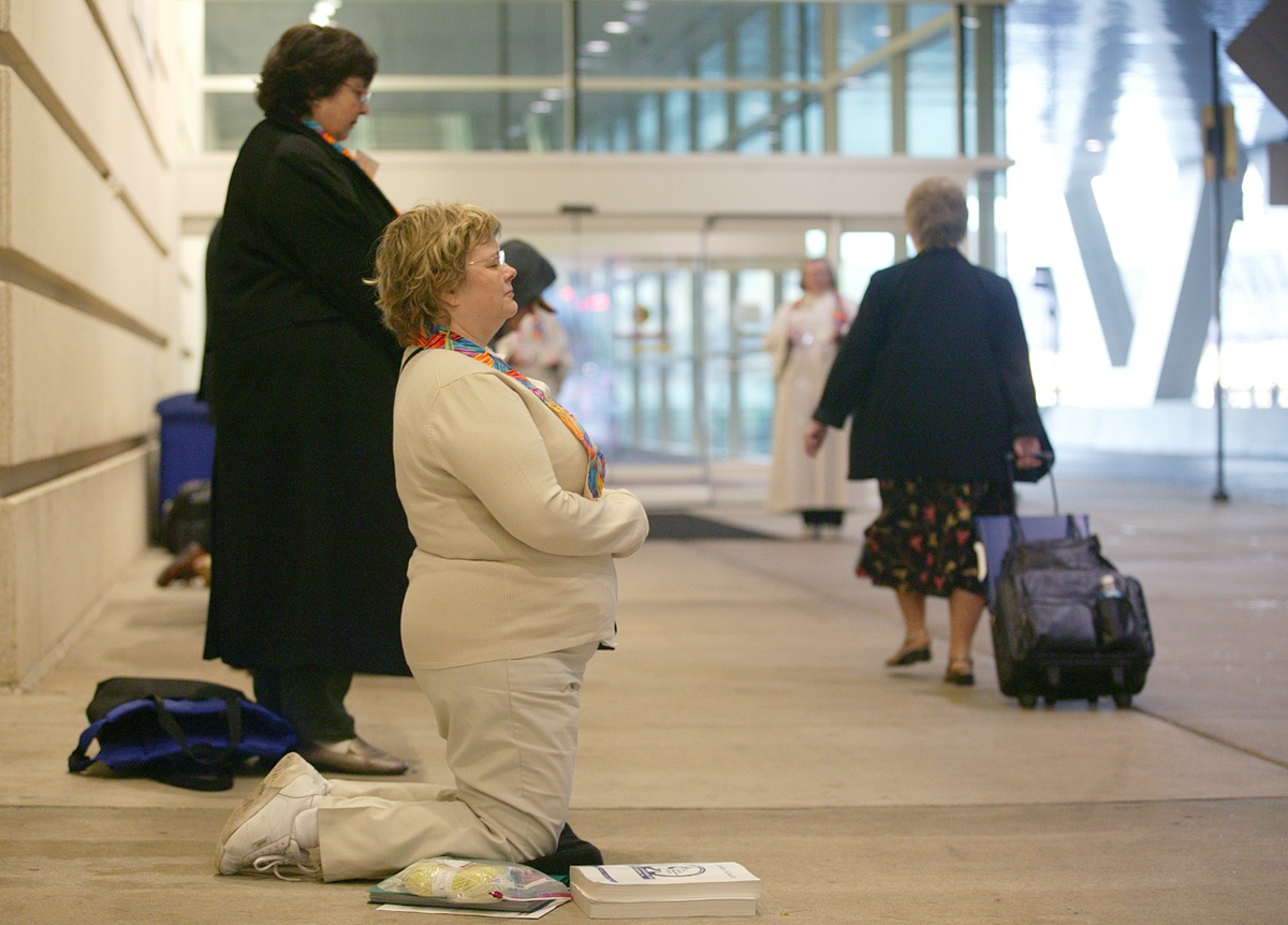 Anne Lewis of Woodland Park United Methodist Church, Seattle, Wash., kneels in silent support of changing the denomination's stance on homosexuality while delegates to the church's 2004 General Conference file into the David L. Lawrence Convention Center in Pittsburgh, PA. A UMNS photo by Mike DuBose.