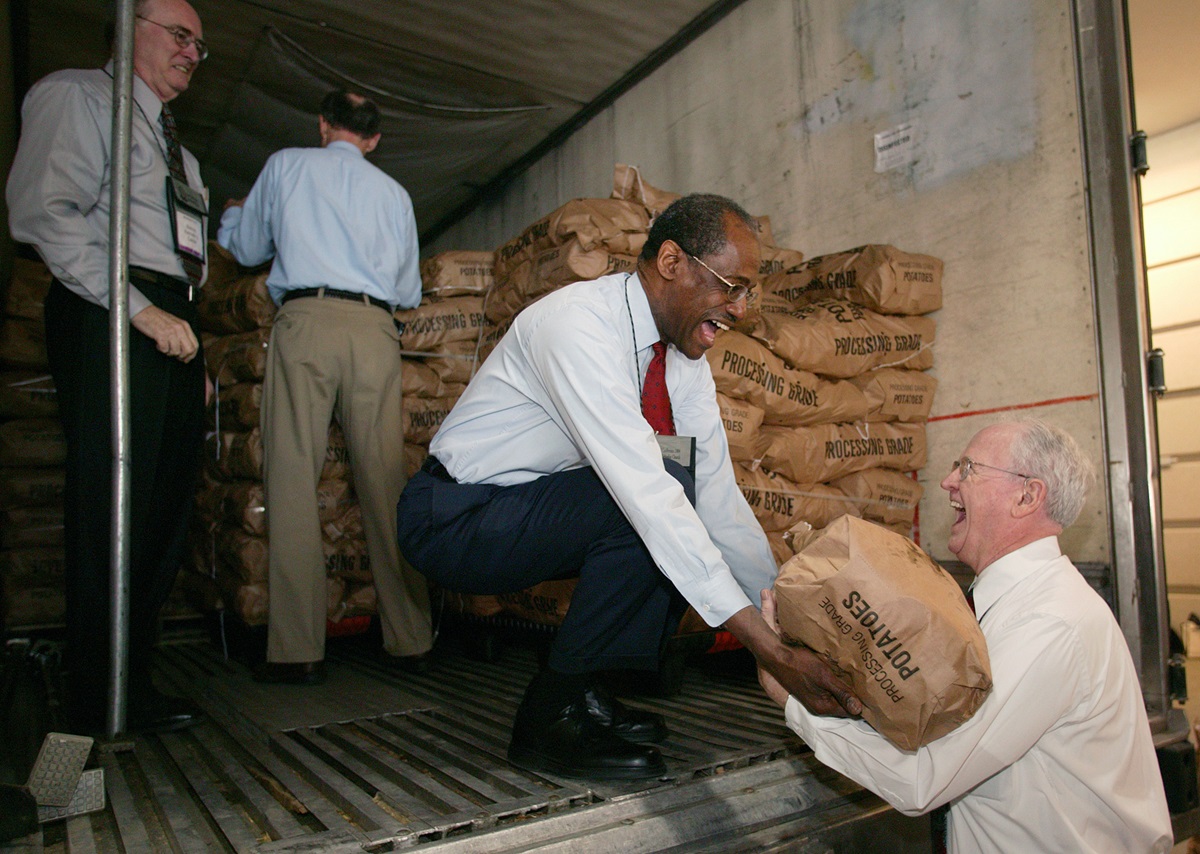Bishops Ernest S. Lyght (kneeling) and Raymond Owen (right) share a laugh while helping to unload 45,000 pounds of potatoes. A UMNS photo by Mike DuBose.