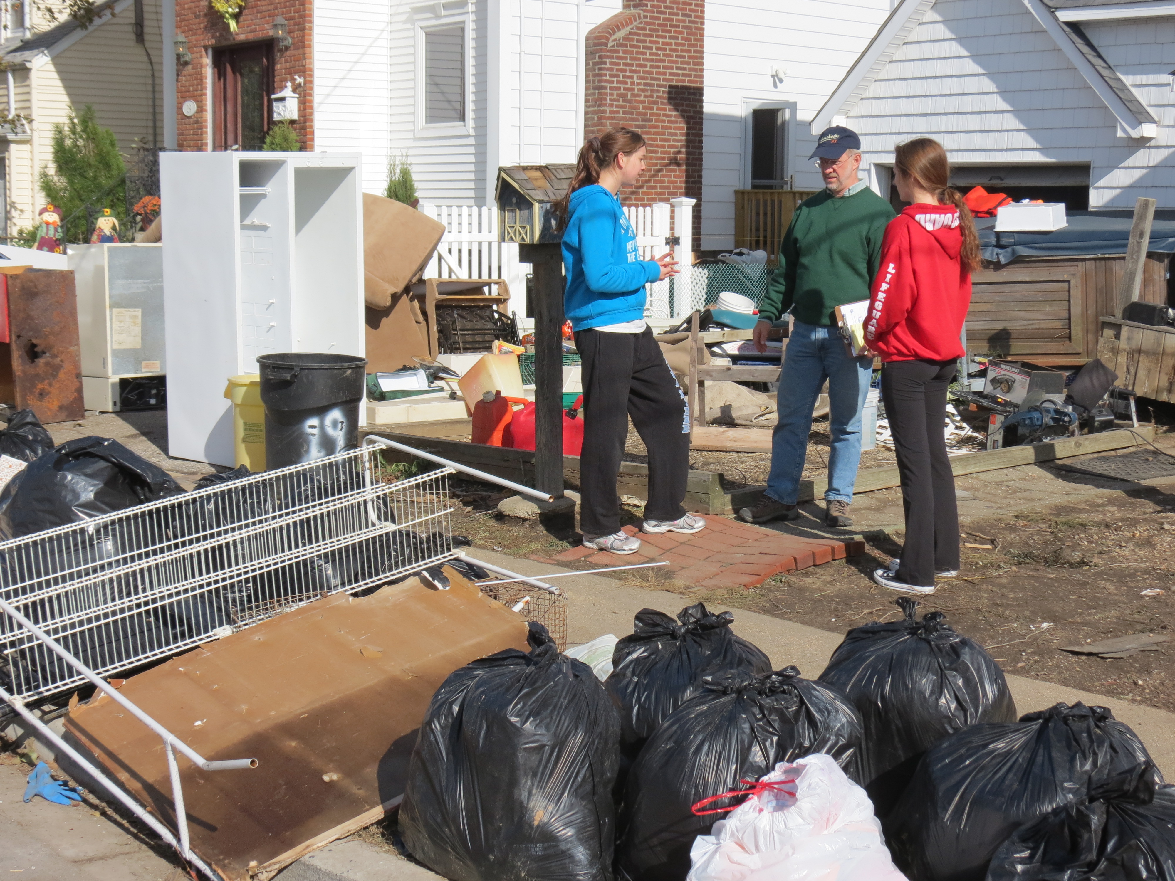 Rev. Jeff Wells, in green, checks in with one of his youth group members and her friends in front of the teen’s storm-damaged home in Massapequa, N.Y. on November 3.