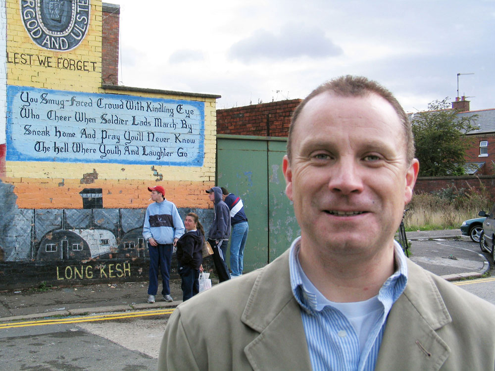 The Rev. Gary Mason, minister at the East Belfast Mission, stands in front of militaristic mural being painted over with an image that celebrates local culture and achievements. A 2003 UMNS file photo by Kathleen LaCamera