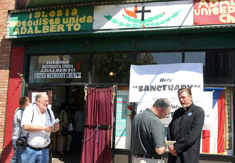 The Rev. Walter Coleman (right), pastor of Adalberto United Methodist Church, is interviewed by news reporters outside the Chicago church's storefront entrance in 2006. Church member Flor Crisóstomo from Mexico has taken refuge in Adalberto, which provided sanctuary to another member last year. A UMNS file photo by Linda S. Rhodes.