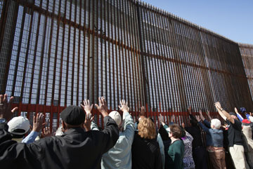 United Methodist bishops raise their hands in prayer in El Faro Park on the Mexican side of the border fence in Tijuana during the May 7 immersion experience.