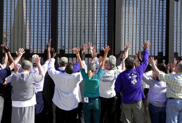 United Methodist bishops raise their arms in prayer next to the border fence in San Diego's Friendship Park. Other bishops do the same on the opposite side of the fence in Tijuana's El Faro Park. A UMNS photo by Karen Clark Ristine.