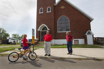 Ashley Kelley, 10, stops by the former Belmore (Ohio) United Methodist Church on her bicycle to ask the Rev. Tom Graves (center) and Ben Smith when the church might reopen. A UMNS photo by Mike DuBose.