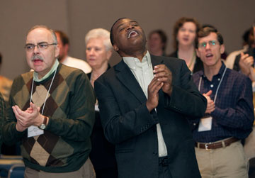 Mike Bella (left) and the Rev. Maidstone Mulenga join in worship during The United Methodist Church's pre-General Conference news briefing. A UMNS photo by Mike DuBose.