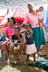 Families share temporary living space beneath a tarp made from a billboard in Petit-Goâve, Haiti. Seated are: Sonia Jean with her daughters Milord Missoule and Fadianie Jean. At rear are Marie Denise Lemaine and her son Samuel. A UMNS photo by Mike DuBose.