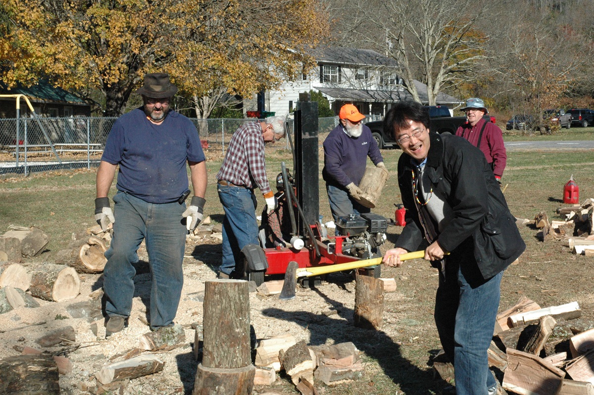 Bishop Jeremiah Park of the Harrisburg Area takes a swipe at chopping firewood as the Rev. David Anderson watches. Anderson (in the brown hat), pastor at First United Methodist Church of Copperhill, Tenn., is a member of a mission team working at Cherokee UMC this week.. A UMNS photo by Annette Spence.