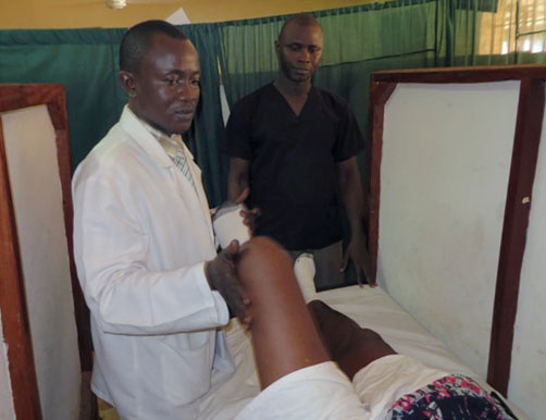 Steven Moinina, head of the unit, helps a patient lift his leg slowly up and down as part of physical therapy. Photo by Phileas Jusu, UMNS.