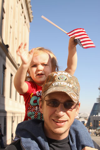 Cadence Cobb, 2, waves an American flag as she rides on the shoulders of her dad, U.S. Army veteran A.J. Cobb