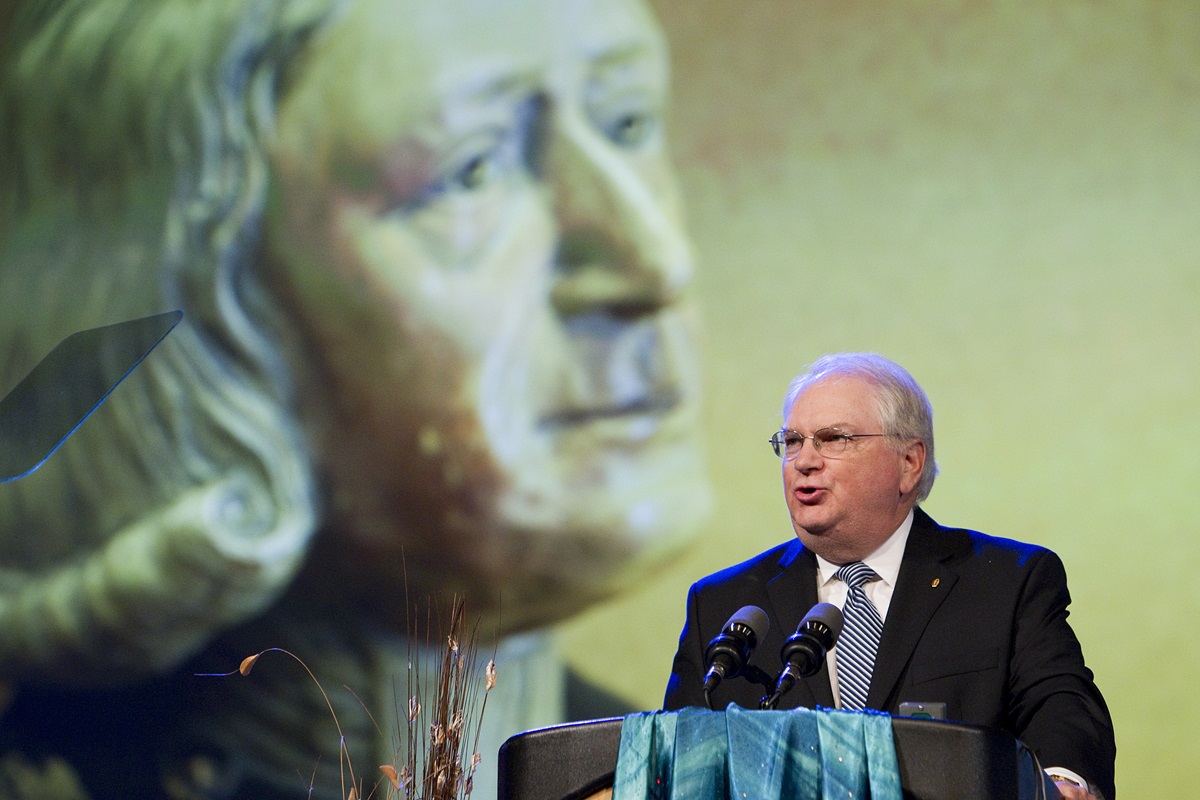 The Rev. Robert J. Williams, backed by a video image of John Wesley, discusses the work of the United Methodist Commission on Archives and History during the denomination's 2012 General Conference in Tampa, Fla. Williams retires Aug 1, 2014. Photo by Mike DuBose, UMNS. 