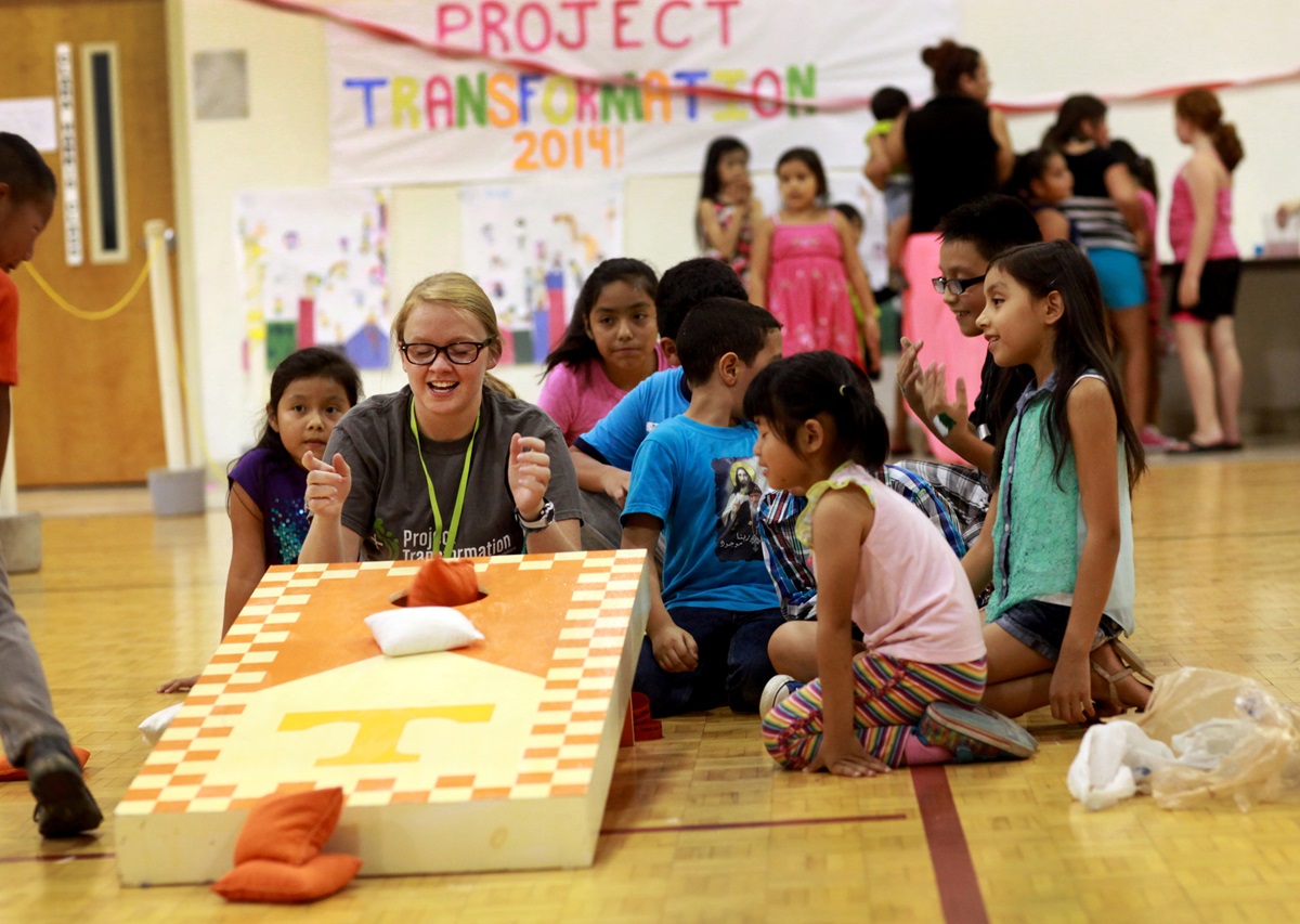 Project Transformation is an eight-week summer camp held in churches creating bonds between the interns and the children they serve. Challye Hays laughs with children as they play corn hole in the gym at Antioch United Methodist Church. 