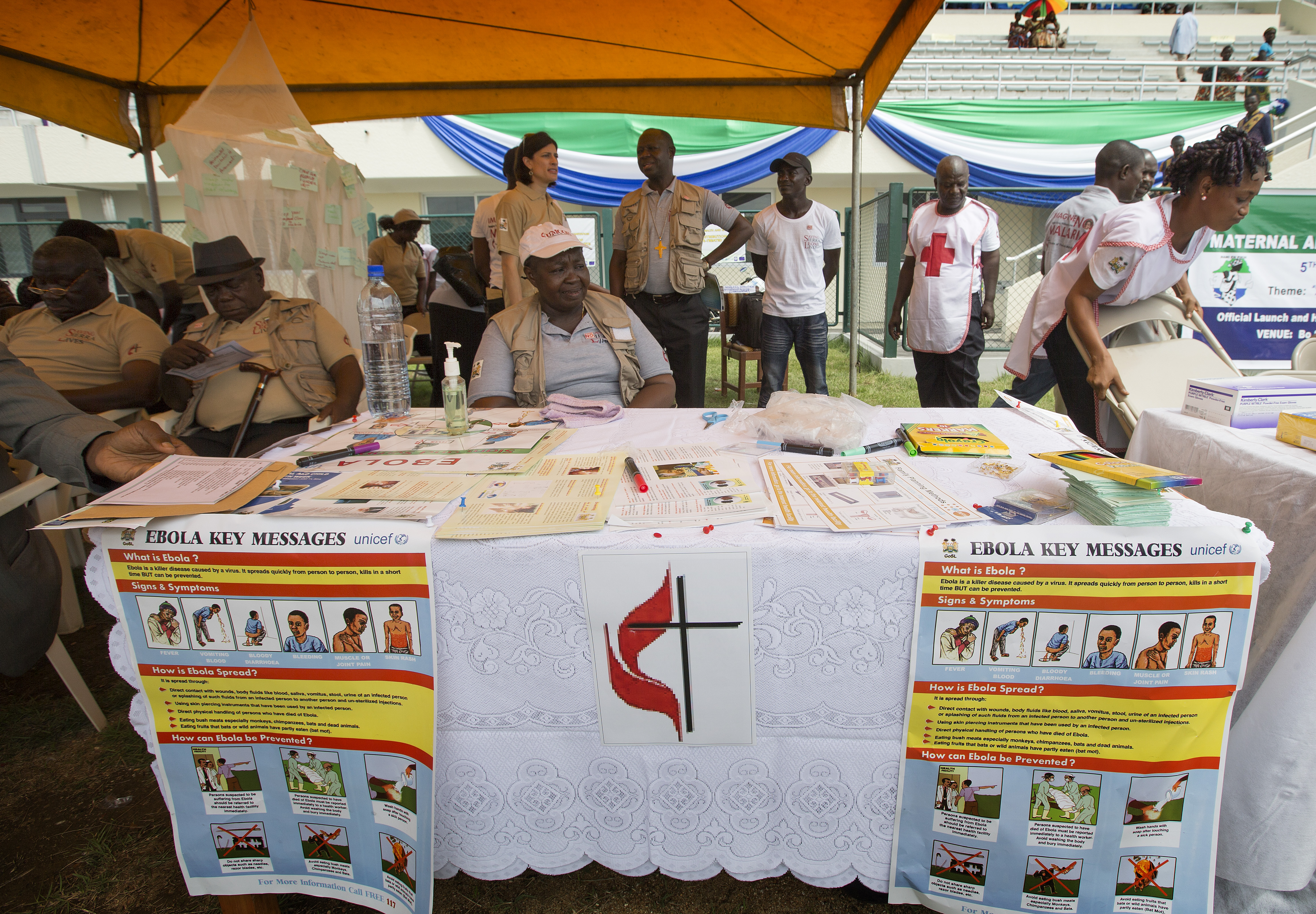 United Methodists, including Beatrice Gbanga (seated at table), medical and health coordinator for the church's Sierra Leone Annual Conference, help spread the word about Ebola during the kickoff for the national Maternal and Child Health Week at the soccer stadium in Bo, Sierra Leone, in June. 