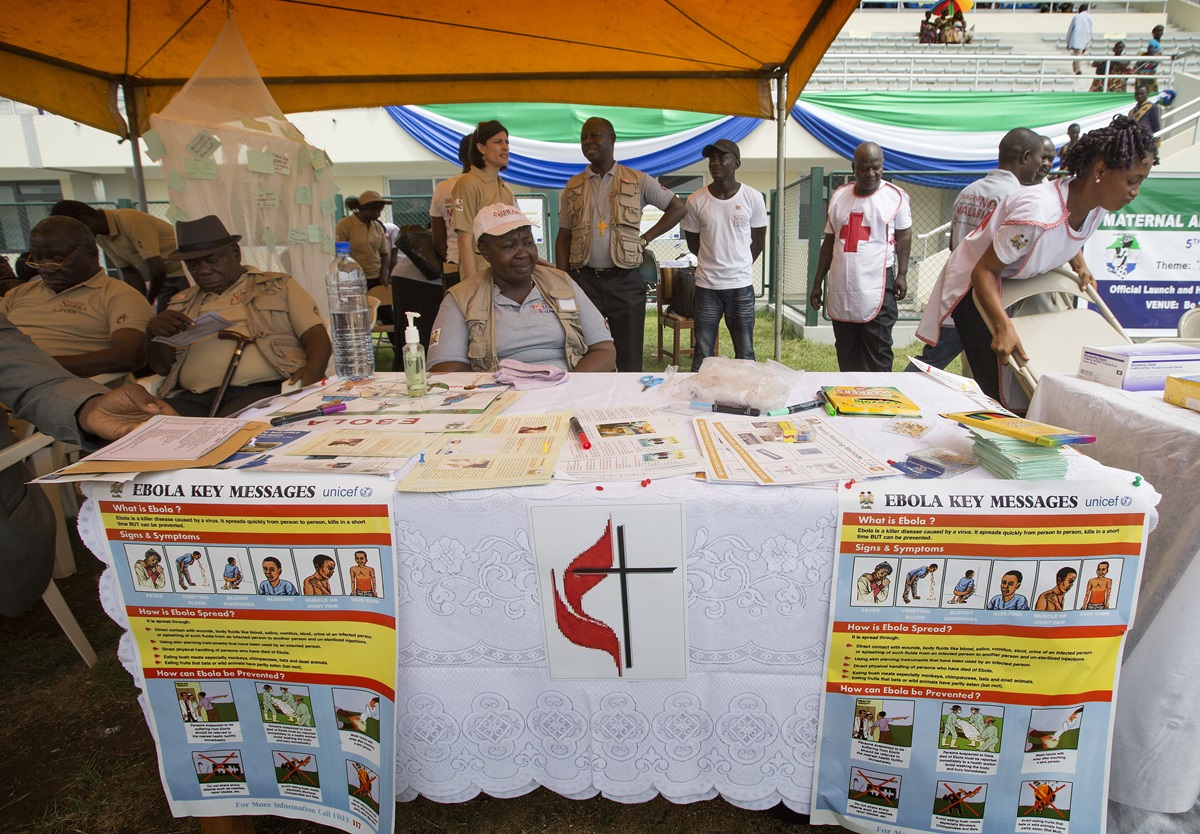 United Methodists, including Beatrice Gbanga (seated at table), medical and health coordinator for the church's Sierra Leone Annual Conference, help spread the word about Ebola during the kickoff for the national Maternal and Child Health Week at the soccer stadium in Bo, Sierra Leone, in June. 