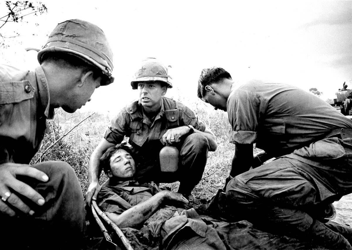 United Methodist Chaplain William “Tom” Carter (center), age 26, helps an injured man whose truck hit a mine 30 miles north of Saigon, Vietnam. Carter added the cross to his helmet with a grease pencil. 