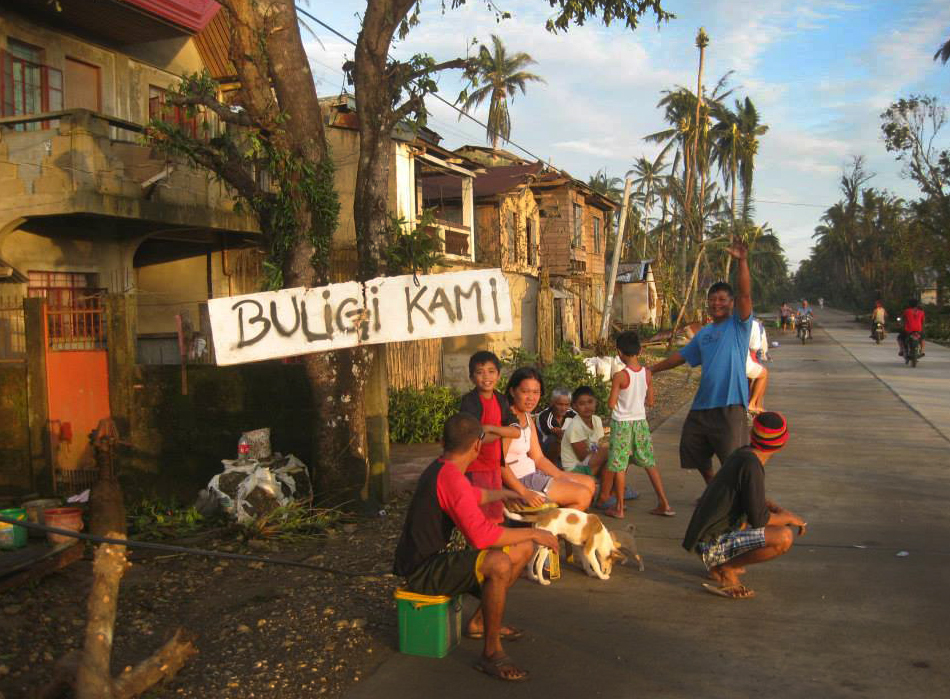 After Typhoon Hagupit, a family in Taft in the province of Eastern Samar sits by a sign that says buligi kami, which translates “Help us please.” Photo by Marlon Paano Lasaca
