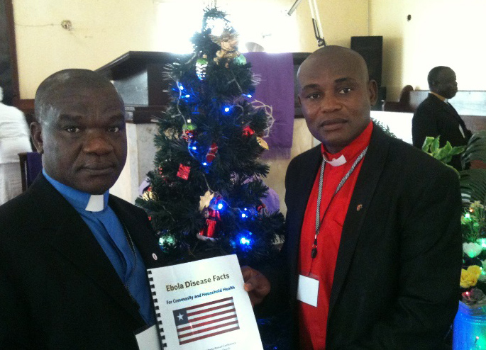 The Rev. Samuel Brown, superintendent of the Monrovia District, and the Rev. Alex Harmon pose with an Ebola Disease Facts Booklet during a book distribution at Tubman United Methodist Church in Paynesville outside of Monrovia. Photo by Julu Swen, UMNS