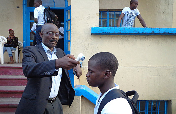 Richard Wiah, president of the College of West Africa, a United Methodist school, checks the temperature of student before he enters the classroom.