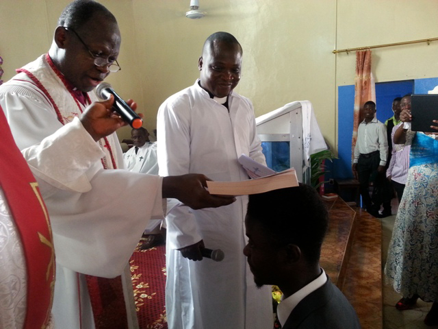 In this file photo, Bishop John K. Yambasu uses a Bible instead of laying on of hands during the induction of clergy as deacons and elders due to the Ebola outbreak. Senesie Rogers is being inducted as interim young adults president.