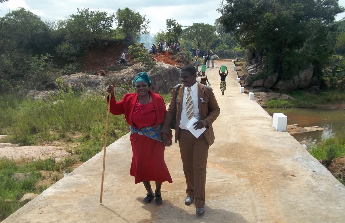 Taurai Emmanuel Maforo assists Keresia Muzaruwetu in crossing the new Chitora-Gwarada Bridge in Zimbabwe. Photo courtesy of Zimbabwe East Conference.