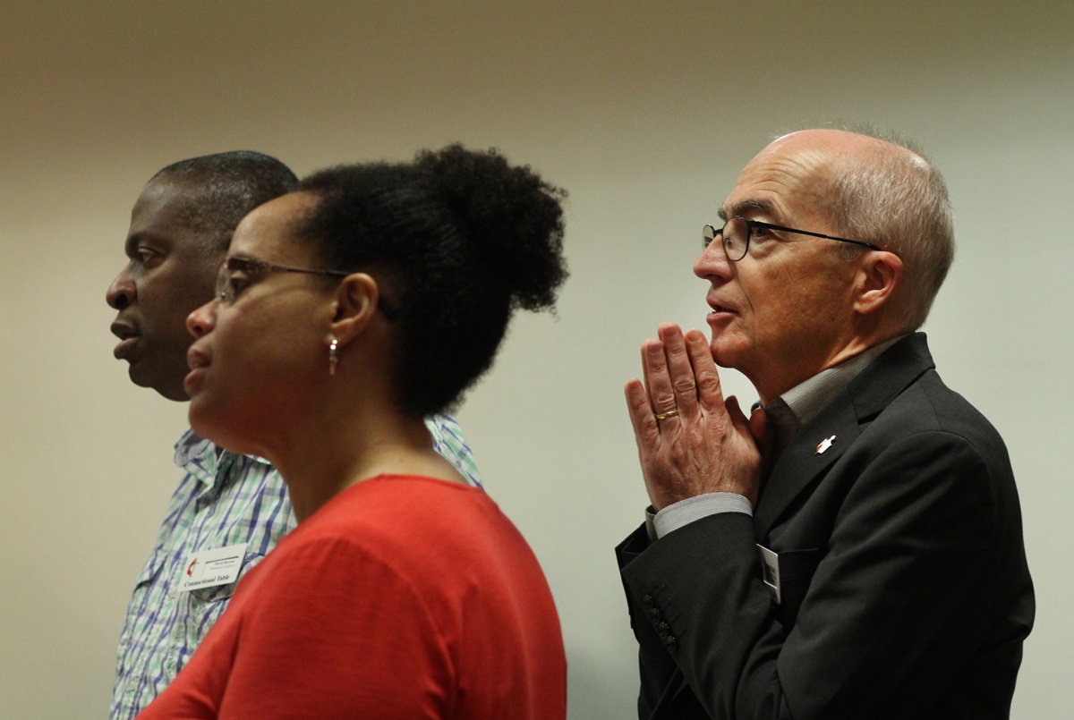 Bishop Patrick Streiff prays during the meeting of the Connectional Table. Standing in front of him are the Rev. Darryl Barrow from the Northeastern Jurisdiction and the Rev. Clarenda Phillips from the Southeastern Jurisdiction. Photo by Kathleen Barry, UMNS