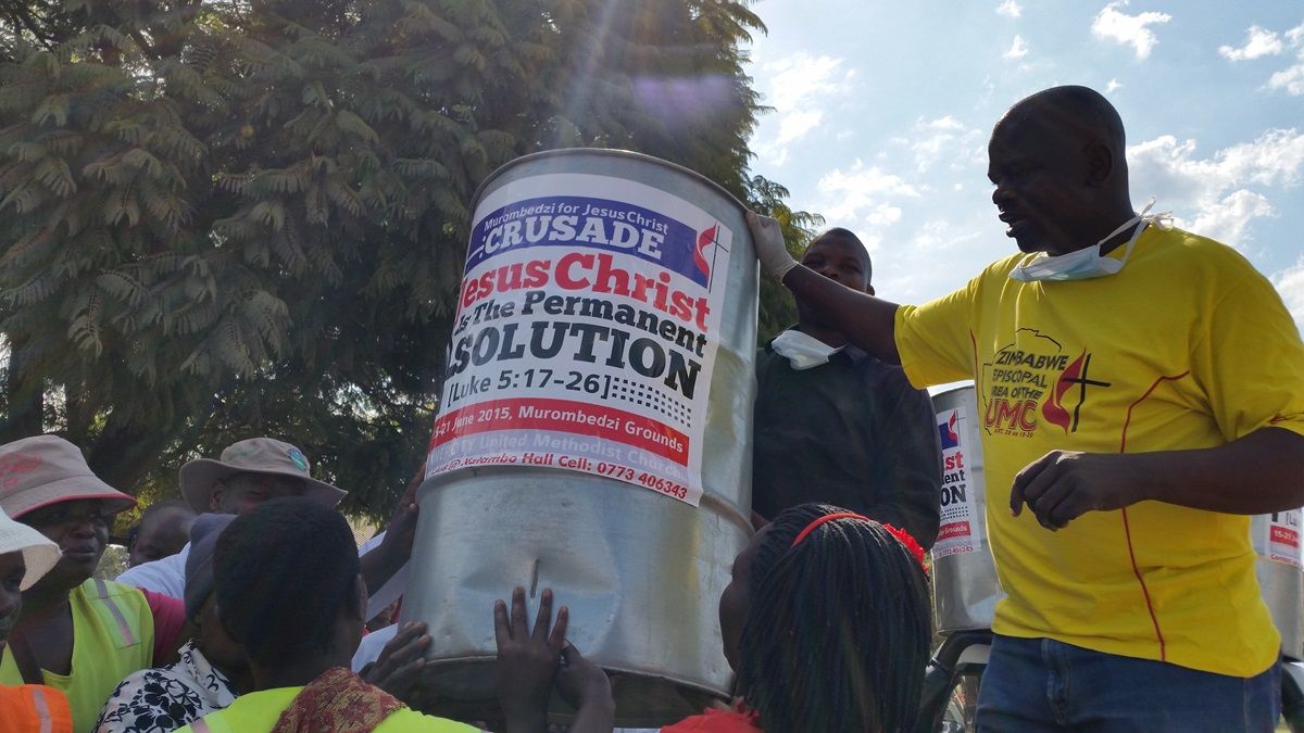 Pastor Taurai Emmanuel Maforo presents a metal litter bin to vendors in  Murombedzi, Zimbabwe. More than 100 members of Murombedzi United Methodist Church joined volunteers from Harare Inner City United Methodist Church, environmentalists and government authorities in an environmental cleanup.  Photo by Eveline Chikwanah, UMNS