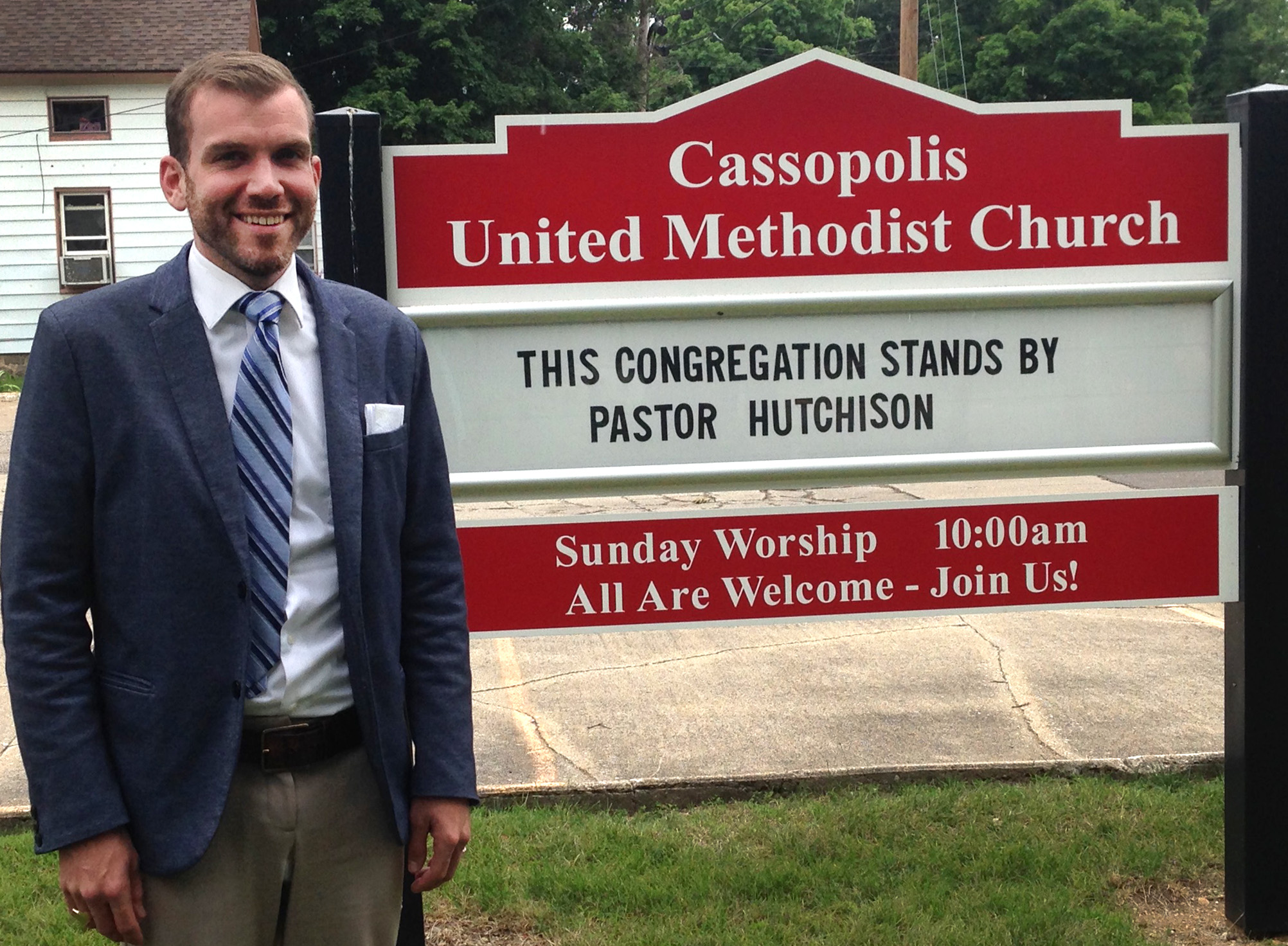 The Rev. Benjamin David Hutchison stands by the sign of Cassopolis United Methodist Church where he served as pastor for two and a half years. He recently was forced to resign from his post at the church against the congregation's wishes. Photo courtesy of Benjamin David Hutchison