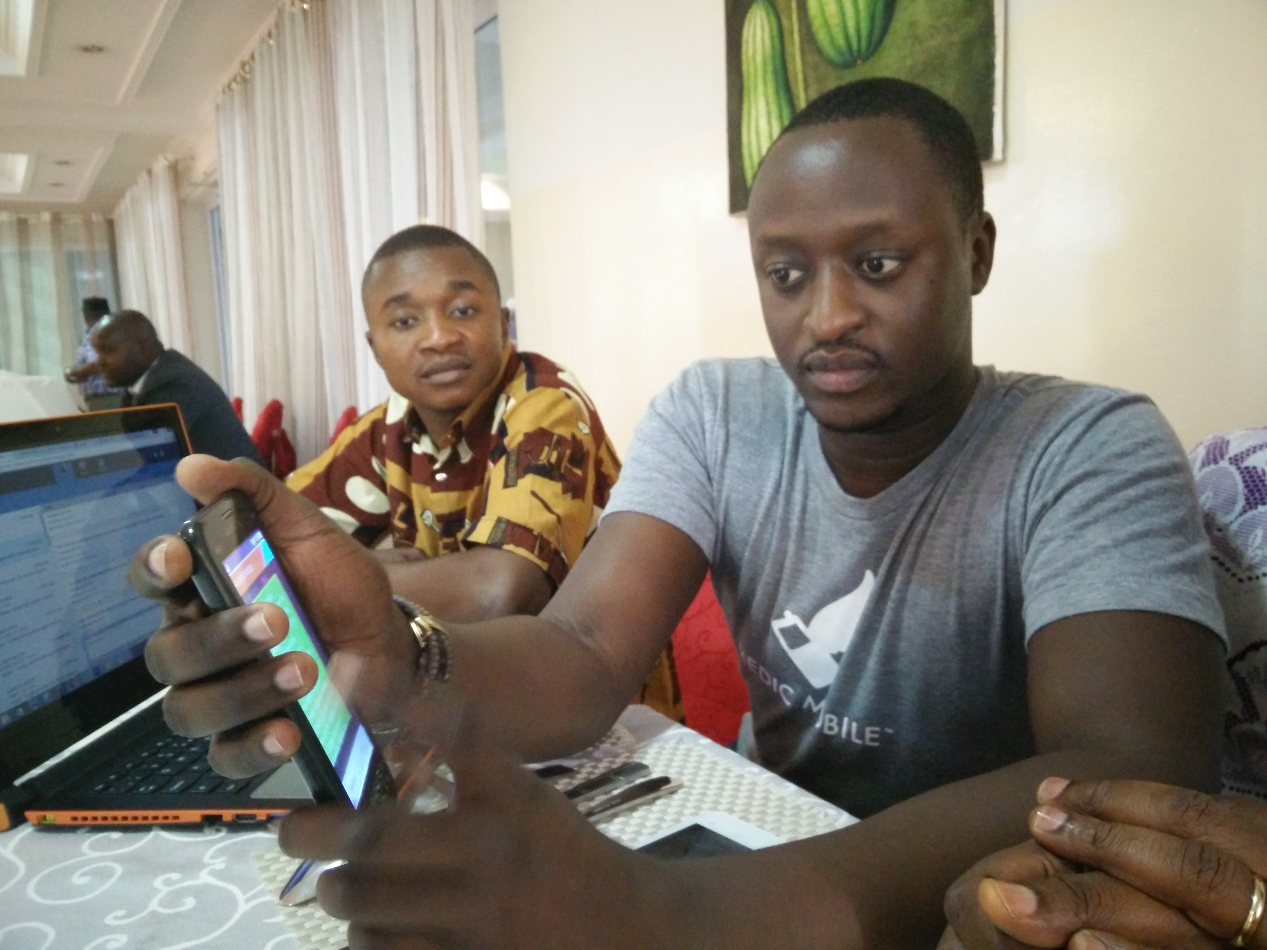 Julio Malikane, right, program director of Medic Mobile, demonstrates the text messaging system used by community health workers. Phillippe Kituka Lolonga, the East Congo Conference communicator, looks on. Photo by Neelley Hicks, UMNS