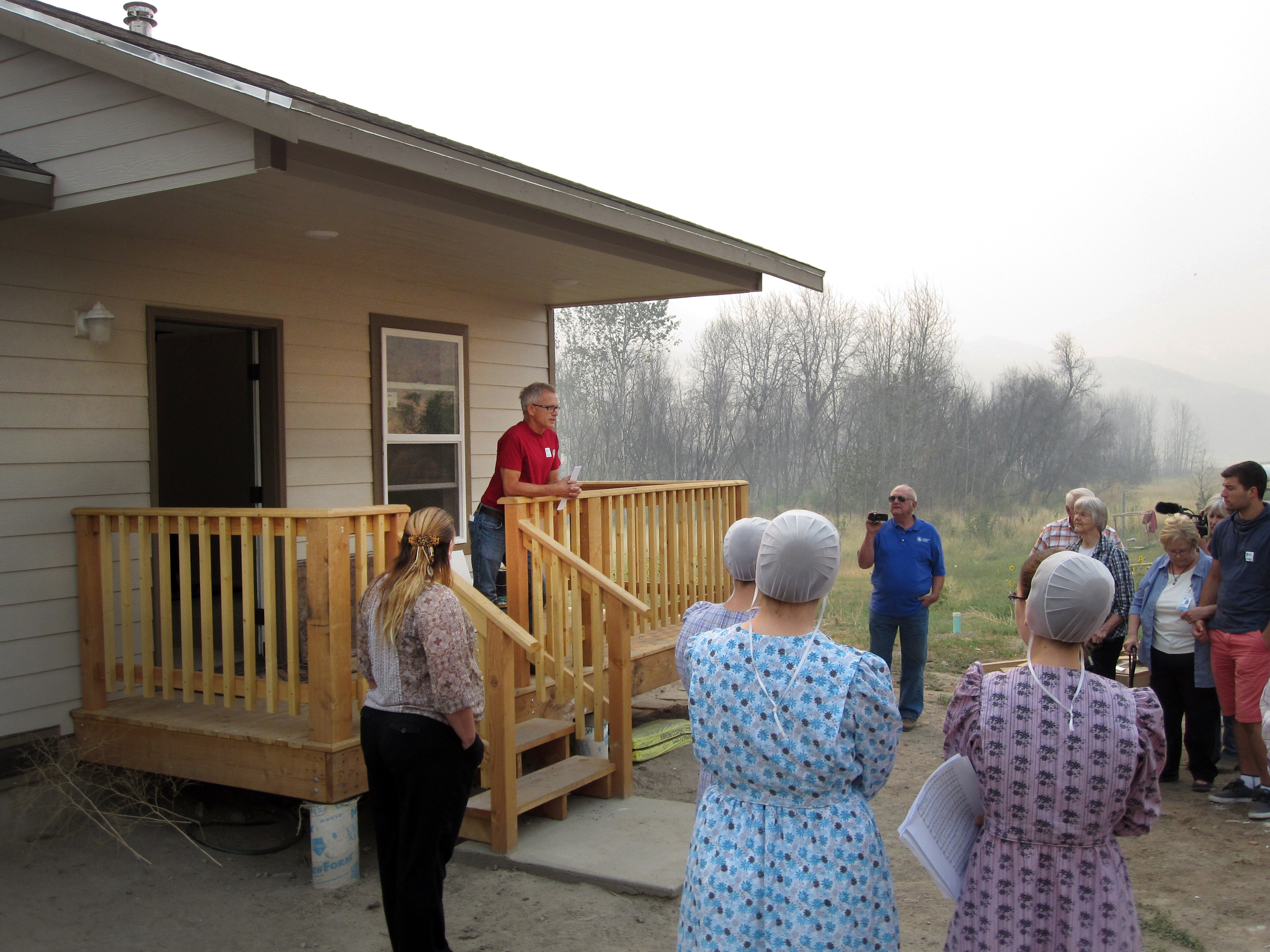Kevin Froese, on deck at left, of Mennonite Disaster Service, speaks during the Aug. 23 dedication of the first of 11 houses to be completed by ecumenical volunteers after last year’s Carlton Complex Fire in Washington. The house was framed by the Amish from Montana, the MDS and United Methodists finished the interior. Photo by Jim Truitt