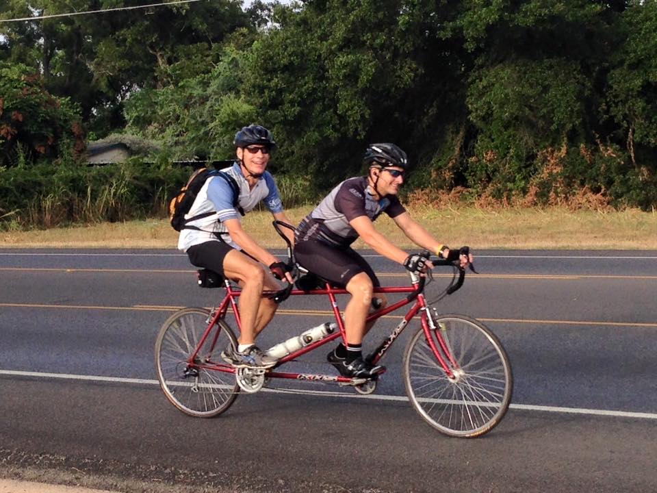 The Rev. Paul Escamilla, pastor of Saint John’s United Methodist Church in Austin, Texas, rides in back while church member Toby Sudduth captains a tandem bike on Friday, Sept. 4 near Bastrop, Texas. Church members are joining Escamilla, who recently fractured his clavicle, in working toward riding 670 miles for the church’s 67th anniversary and in turn raising funds for mission. 
