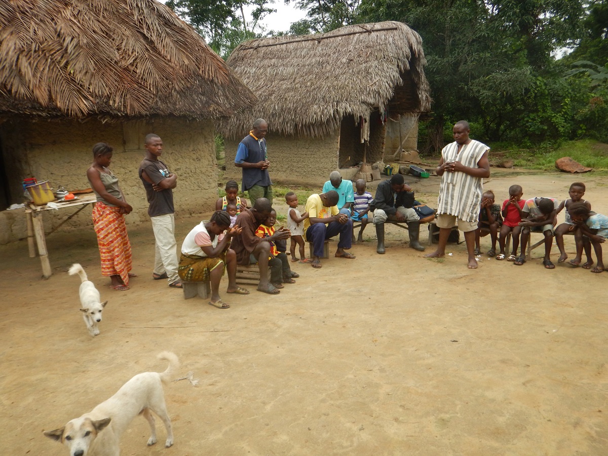 Kowama Village chief and pastor Joseph Tommy (third standing from left) leads prayers before the community meeting starts. Photo by Phileas Jusu, UMNS