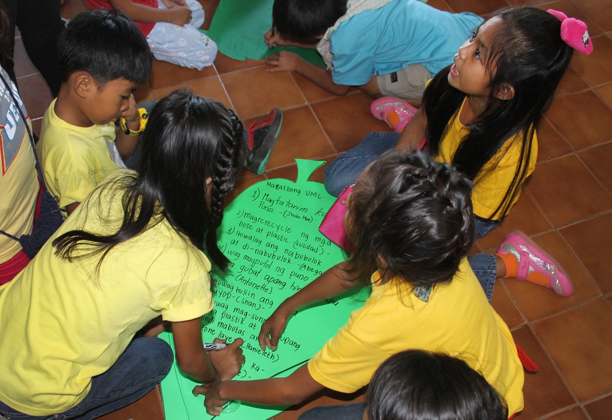 Filipino children ages 5 to 12 write ways they can help reduce the Earth’s temperature. Examples (written on green paper leaves) include avoiding smoking, planting more trees, conserving water and electricity, recycling plastic and paper.