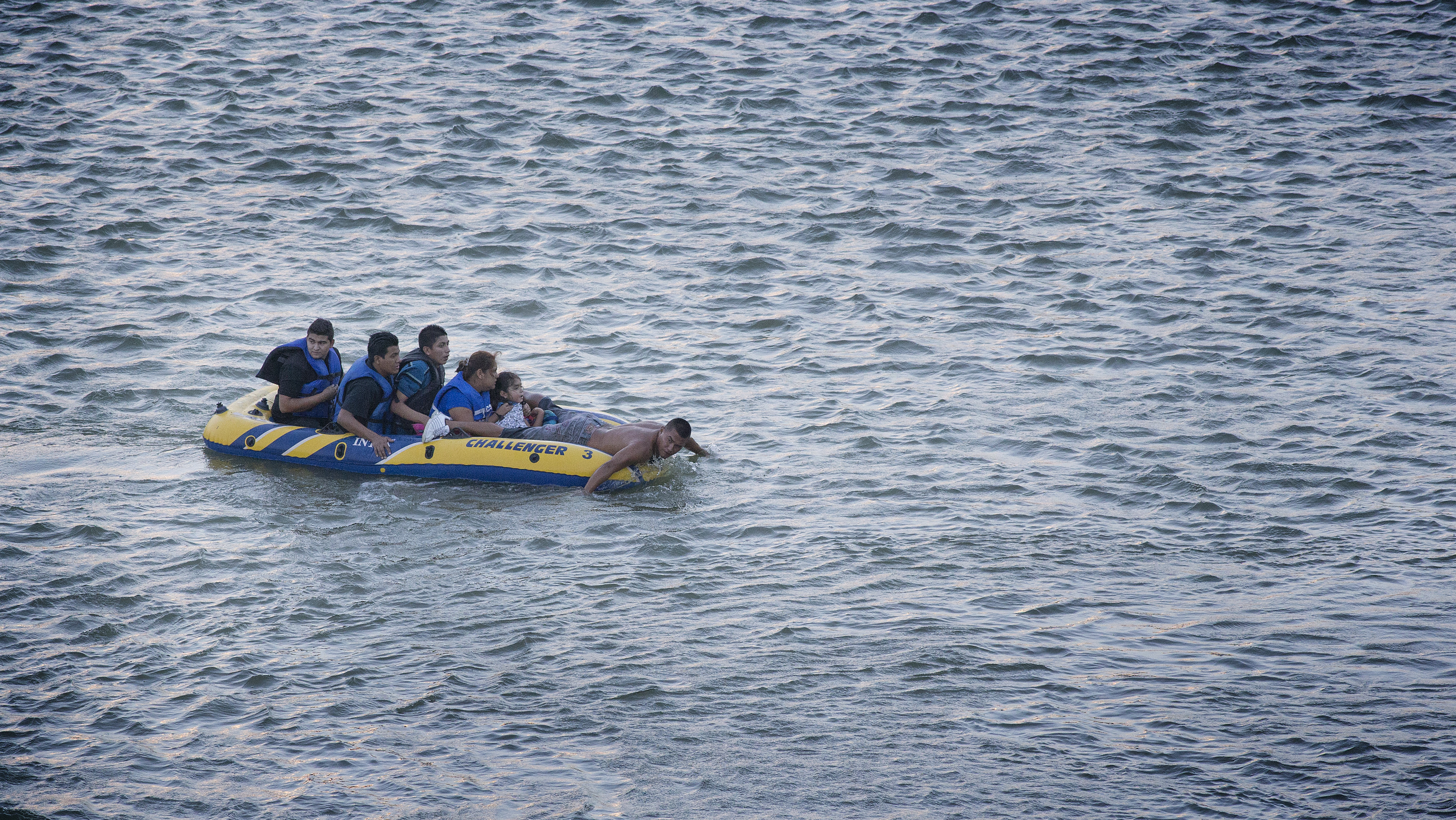 A coyote, or smuggler, (right) uses his hands to paddle a rubber raft full of immigrants across the Rio Grande from Mexico to the U.S. side of the river in Roma, Texas, in August 2014. File photo by Mike DuBose, UMNS