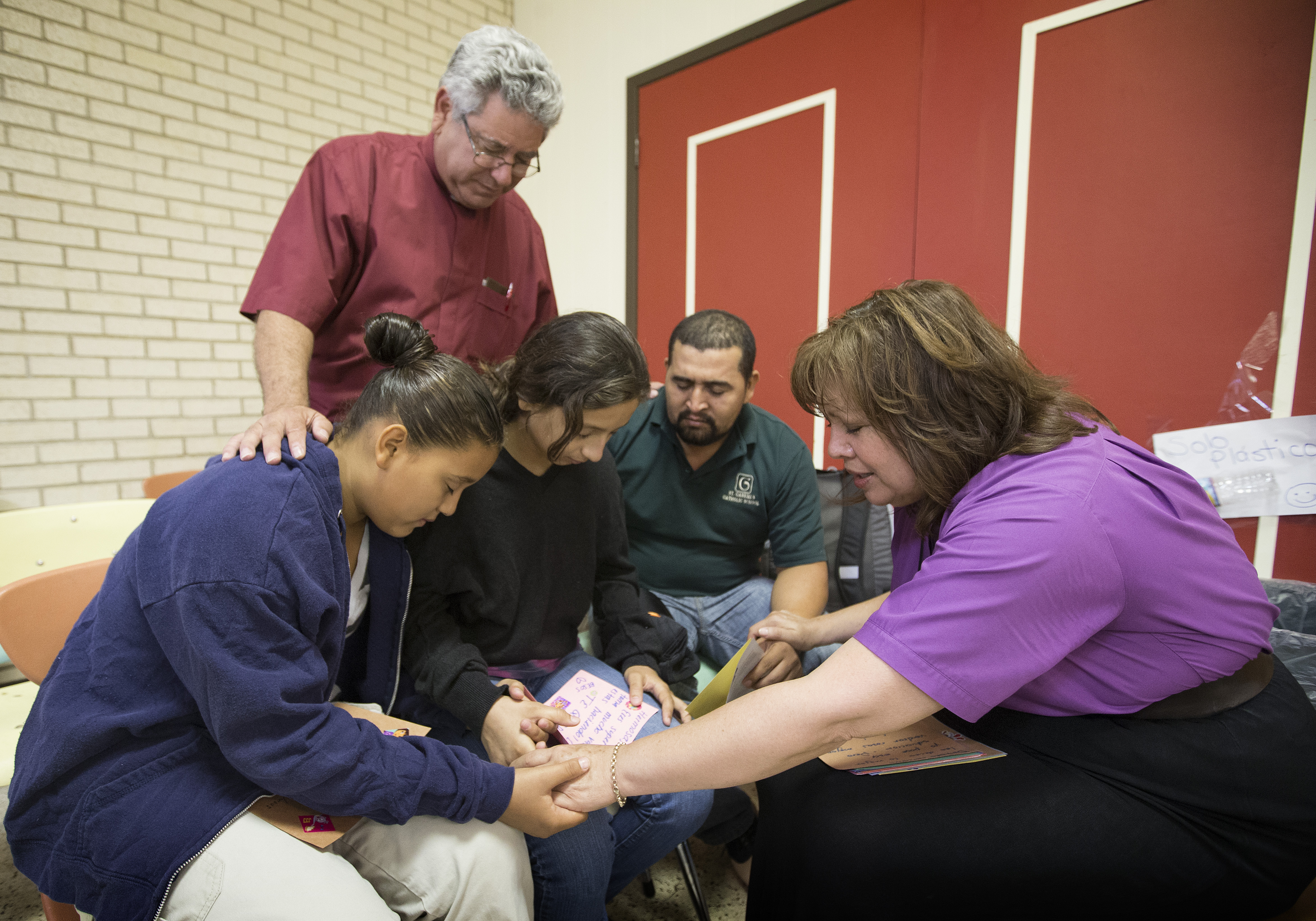 United Methodist Bishop Minerva Carcaño (right) and the Rev. Javier Leyva (standing) pray with Elmer Moreno Gonsales and his daughters Mariela (left) and Katerin at the immigrant welcome center at Sacred Heart Catholic Church in McAllen, Texas. The family immigrated from Honduras following a month-long journey. File photo by Mike DuBose, UMNS