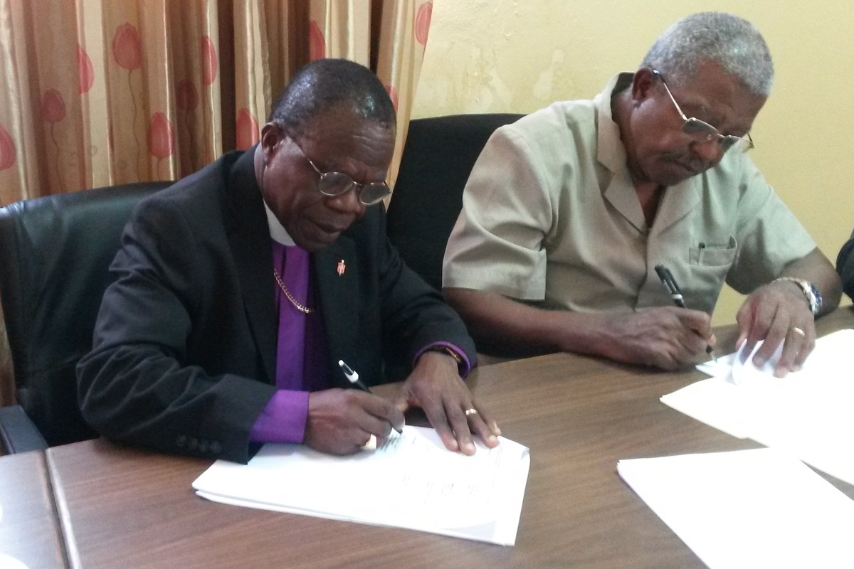 Bishop John Innis signs the construction contract for a commercial building that The United Methodist Church Liberia hopes will generate income to support the ministry of the church. Next to him is John Togba, co-chairman for the Liberia United Methodist Empowerment Foundation. Photo by Julu Swen, UMNS