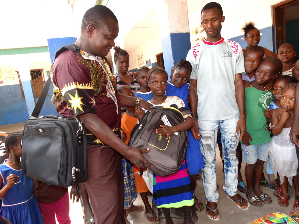 Adamsay Conteh, a student at The United Methodist Church Primary School in Mamaka, Sierra Leone, receives a backpack containing uniforms, books and other materials from Leonard Ben-Gbloa, education secretary for primary schools. Photo by Phileas Jusu, UMNS 