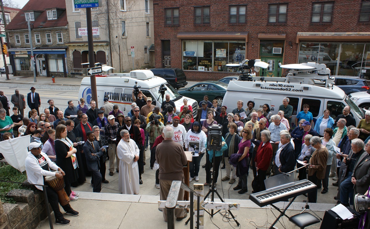 A crowd of more than 200 people of many faiths listens prior to walking through Philadelphia's gun damaged Germantown neighborhood.