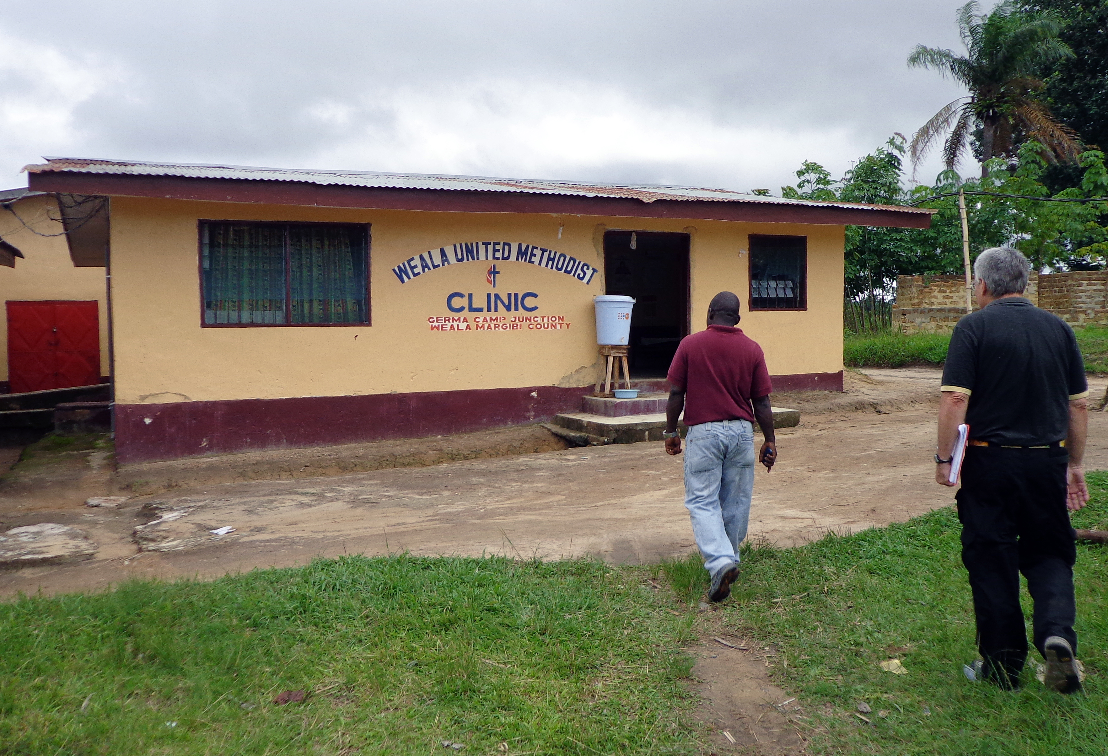 Two men walk toward the Weala United Methodist Church Liberia Clinic. 