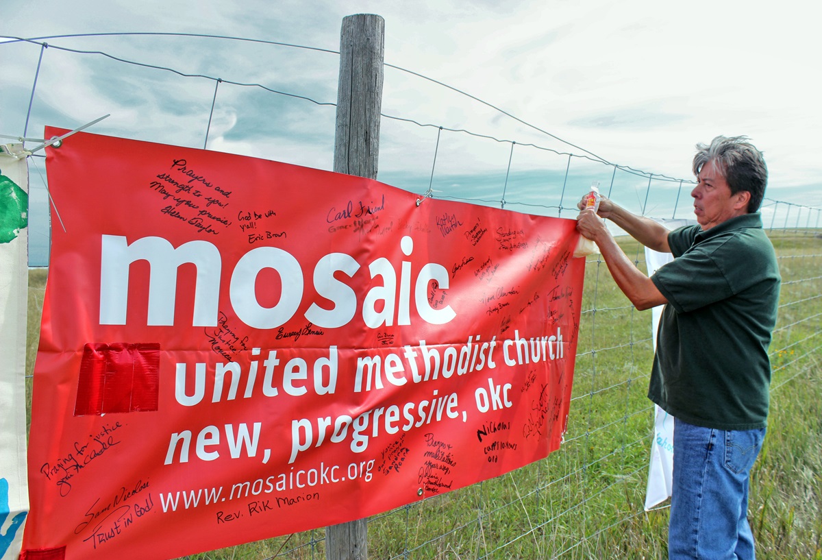 The Rev. David Wilson, superintendent of the Oklahoma Indian Missionary Conference, attaches banners from United Methodist churches supporting the Standing Rock Sioux’ protest of the Dakota Access Pipeline. Wilson was at the protest camp, near Cannon Ball, N.D., on Sept. 10. Other United Methodist pastors will be gathering there for an interfaith clergy event on Nov. 3. 