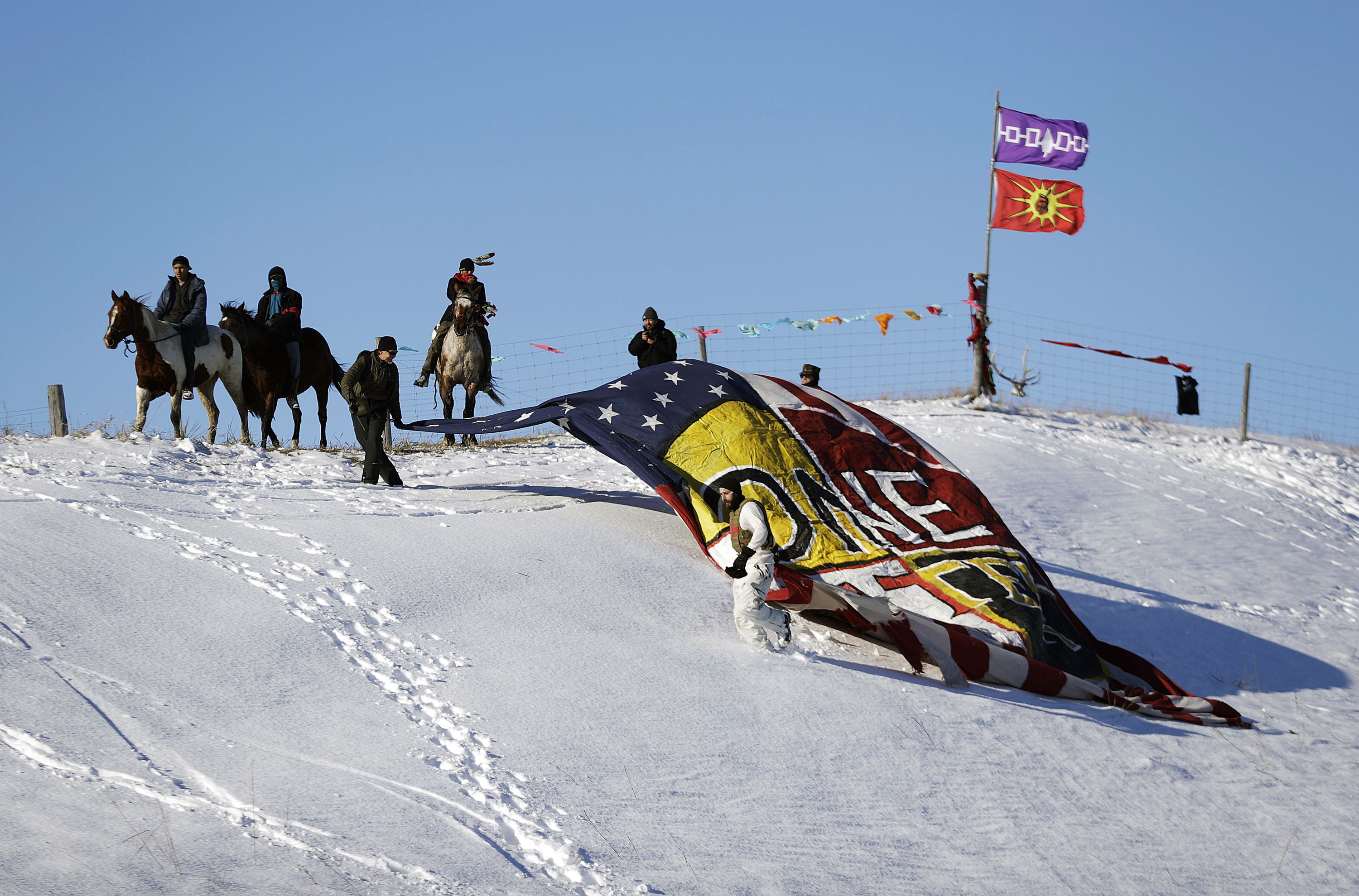 Veterans unveil a banner that reads "One Water" on a hillside across from the Oceti Sakowin camp where people have gathered to protest the Dakota Access oil pipeline in Cannon Ball, N.D., Sunday, Dec. 4, 2016. Tribal elders have asked the military veterans joining the large Dakota Access pipeline protest encampment not to have confrontations with law enforcement officials, an organizer with Veterans Stand for Standing Rock said Sunday, adding the group is there to help out those who've dug in against the four-state, $3.8 billion project. Photo by David Goldman, AP