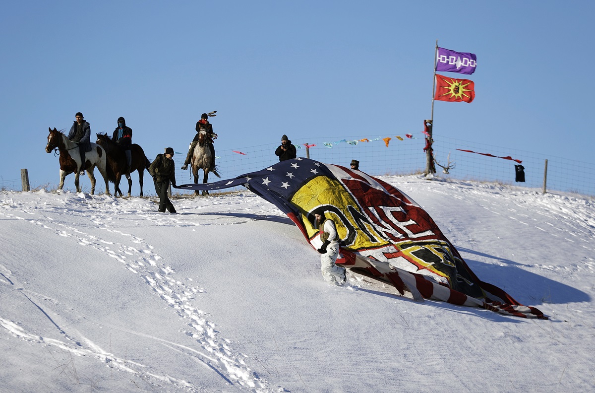Veterans unveil a banner that reads "One Water" on a hillside across from the Oceti Sakowin camp where people have gathered to protest the Dakota Access oil pipeline in Cannon Ball, N.D., Sunday, Dec. 4, 2016. Tribal elders have asked the military veterans joining the large Dakota Access pipeline protest encampment not to have confrontations with law enforcement officials, an organizer with Veterans Stand for Standing Rock said Sunday, adding the group is there to help out those who've dug in against the four-state, $3.8 billion project. Photo by David Goldman, AP