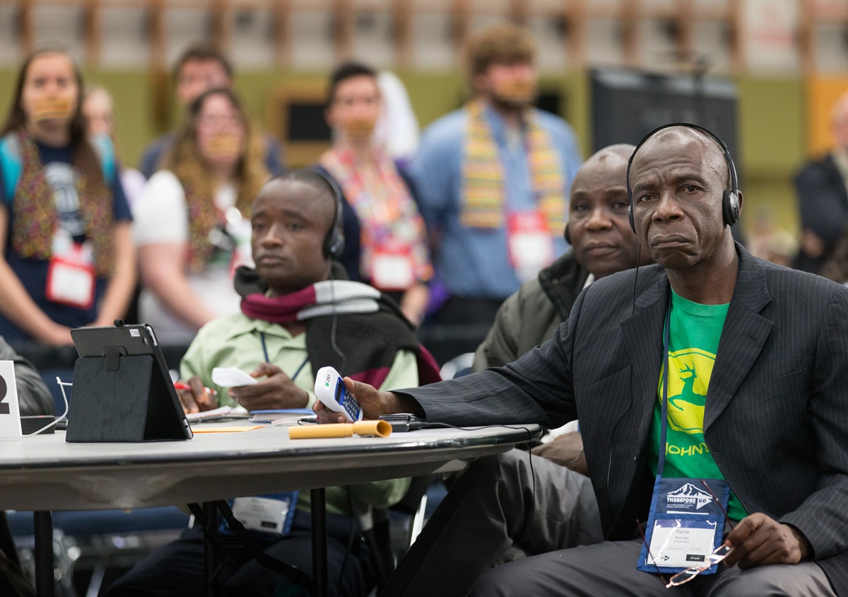 Delegate Pierre Kasongo (right) and other members of the Tanganyika delegation vote on legislation while supporters of full rights for LGBTQ persons in the life of The United Methodist Church stand with their mouths taped shut outside the bar of the 2016 United Methodist General Conference in Portland, Ore., to symbolize the way LGBTQ people feel they are silenced by the church. Photo by Mike DuBose, UMNS.