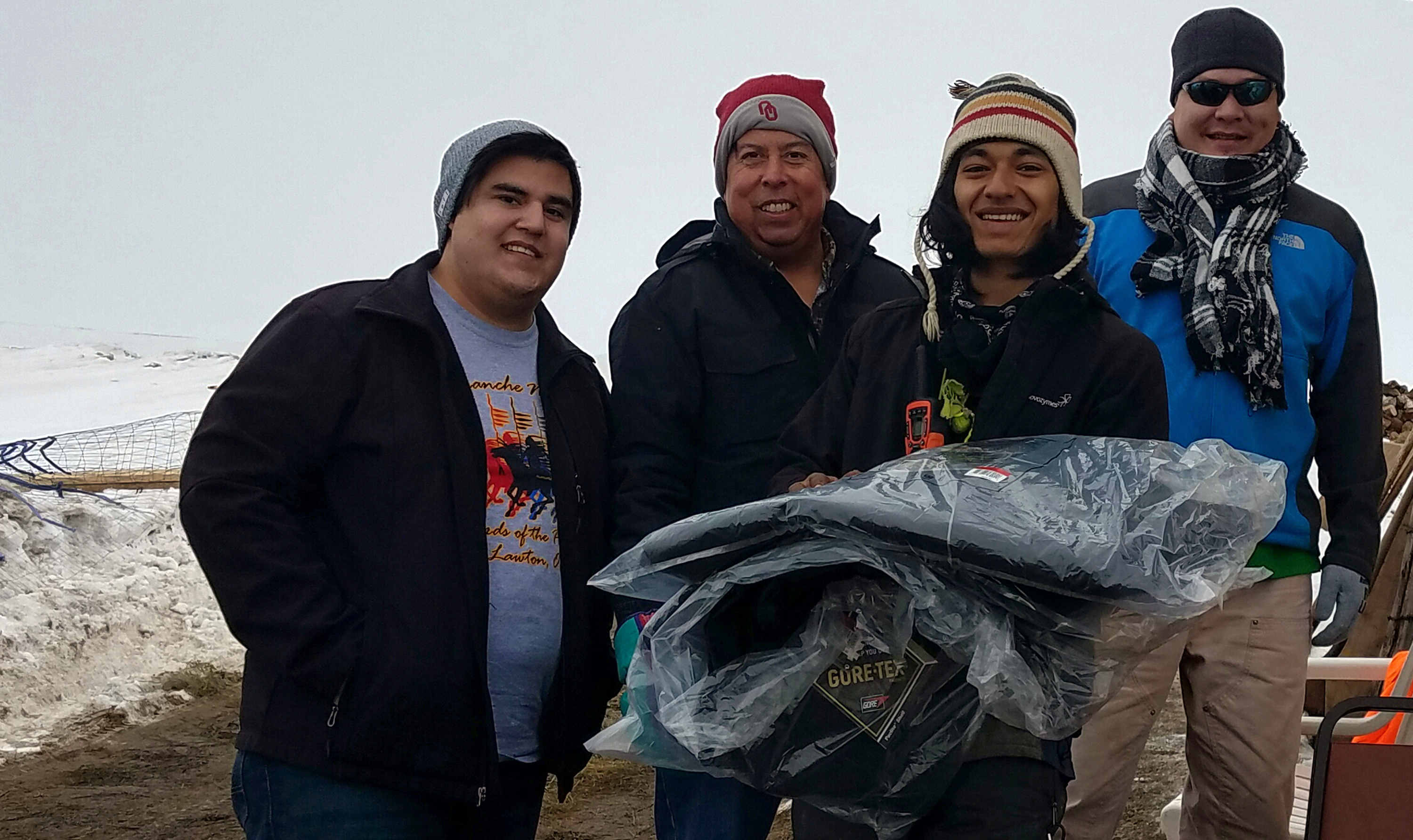 Dallas Parker, left, the Rev. David Wilson and Tim Byington, right, present thermal coats to a camp volunteer at the Oceti Sakawin Camp at Standing Rock. The coats were donated by the Urban Inter-Tribal Center of Texas. Photo courtesy of Dallas Parker.