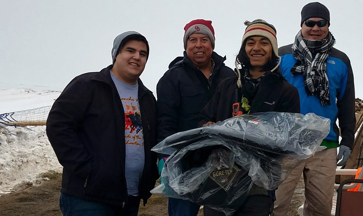 Dallas Parker, left, the Rev. David Wilson and Tim Byington, right, present thermal coats to a camp volunteer at the Oceti Sakawin Camp at Standing Rock. The coats were donated by the Urban Inter-Tribal Center of Texas. Photo courtesy of Dallas Parker.