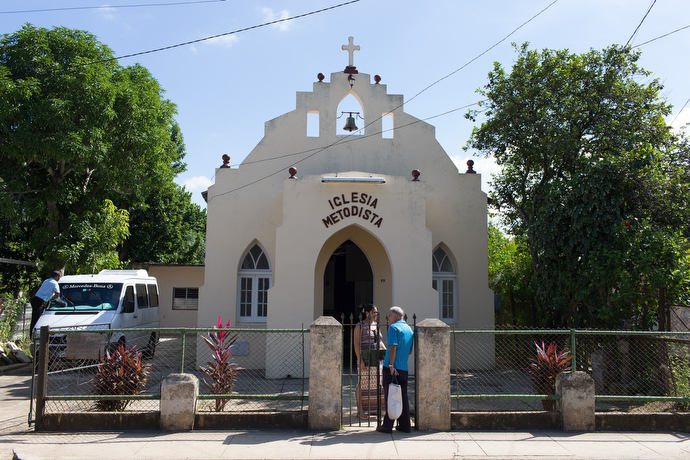 Iliansis Rodriguez (behind fence) greets a neighbor in front of San Antonio Methodist Church in San Antonio de Rio Blanco, Cuba. Rodriguez is the wife of the pastor. Photo by Mike DuBose, UMNS.