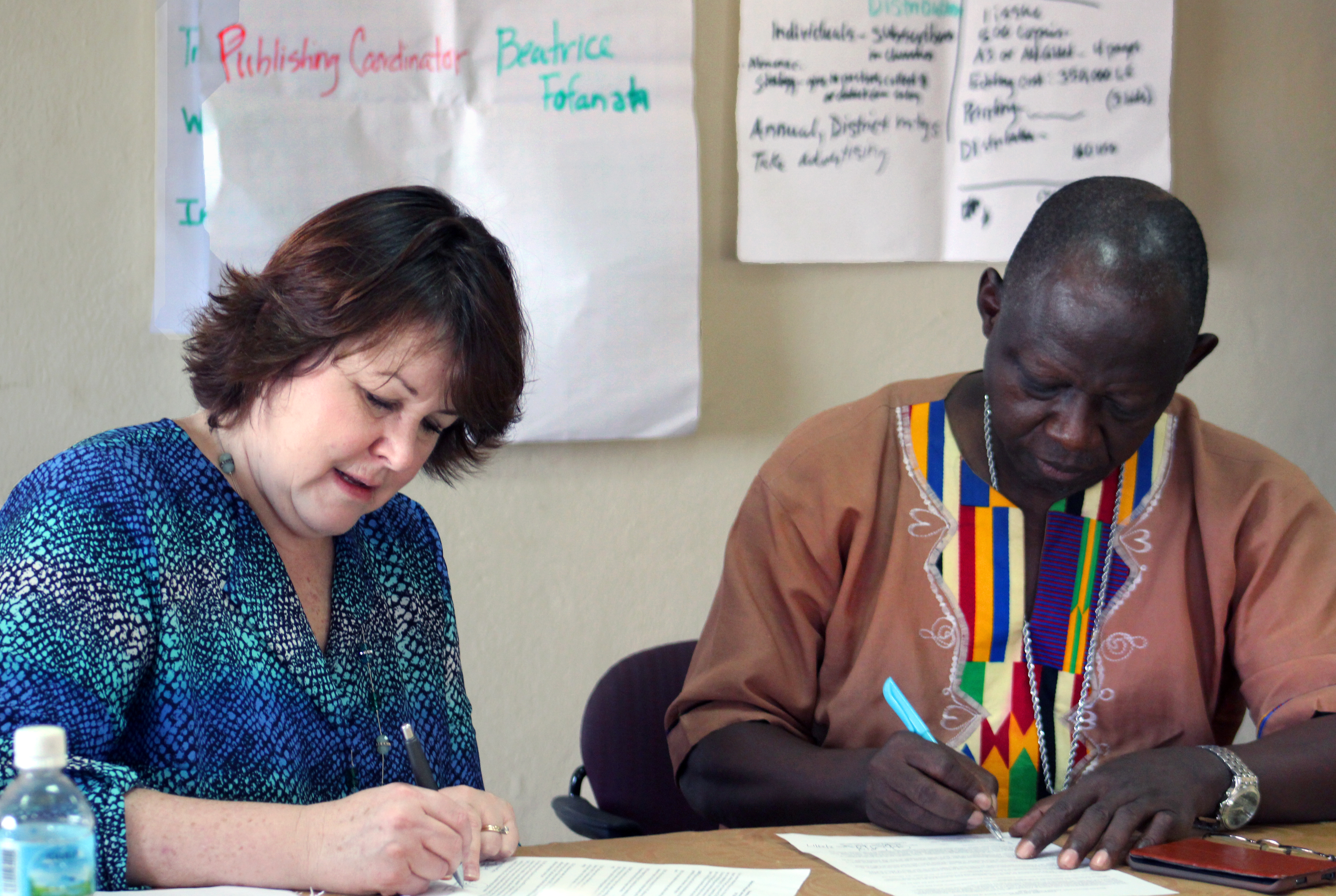 Robin Pippin of Discipleship Ministries, left, and Bishop John K. Yambasu of the Sierra Leone Episcopal Area sign an agreement creating a new publishing team in Sierra Leone. The 12-member team’s first project will be the creation of a quarterly newsletter for sharing information about the church with members. Photo by Julu Swen, UMNS