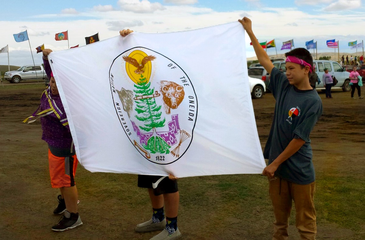 Young people from Oneida United Methodist Church, who attended the Peg-Leg Flamingos youth leadership conference in September, present a tribal flag to water protectors at Standing Rock. Photo courtesy of the Rev. Carol Lakota Eastin