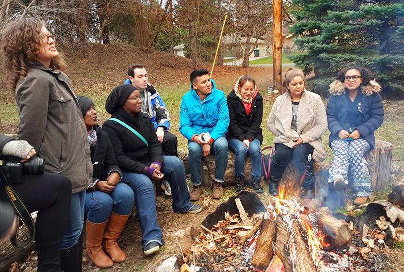 Participants in the 2016 Leadership Training Program in Minneapolis sit around a campfire in the yard of the Fink House, part of the Underground Seminary. The annual training programs are organized by the Student Christian Movement-USA and the World Student Christian Federation-North America. Photo by Luciano Kovacs.