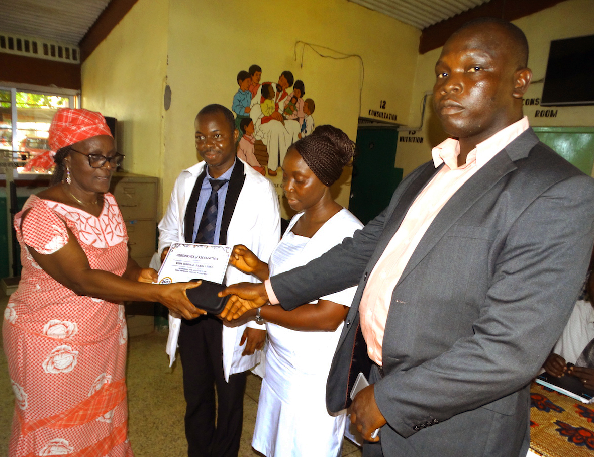 Yeabu Kamara, former chairman of the restructuring committee at Kissy Hospital, hands the certificate of recognition to hospital administrator Joseph Mbogba along with communication gadgets that were part of the award. Photo by Phileas Jusu, UMNS