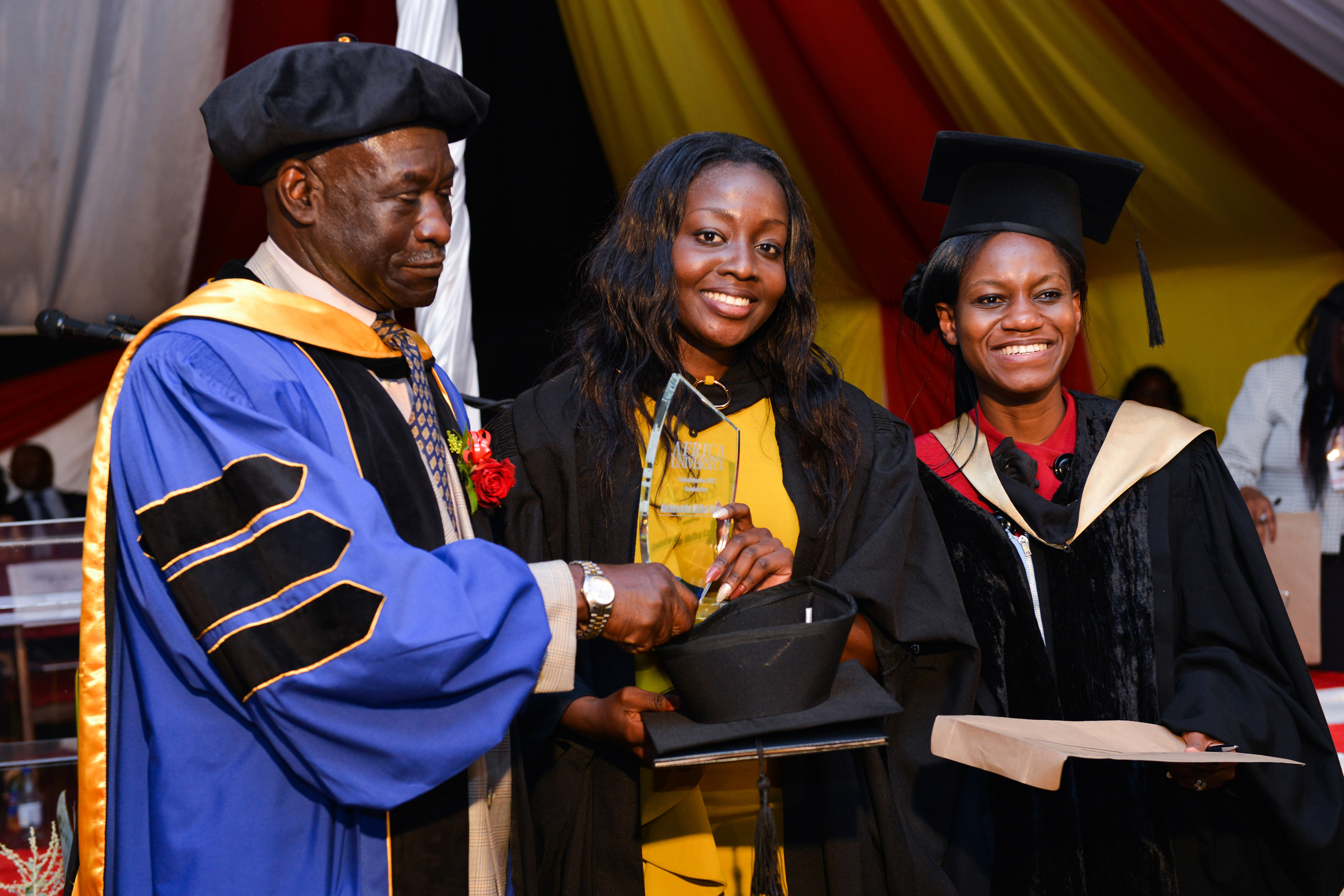 Class valedictorian Kudakwashe Mellisa Kapesa (center) holds a trophy honoring her scholastic achievements during the 2017 commencement ceremonies at Africa University in Mutare, Zimbabwe. Kapesa, who had a cumulative GPA of 3.92, is flanked by the Deputy Vice Chancellor Pro Deputy Vice Chancellor, Professor Ikubolajeh Logan (left) and the Acting Registrar, Miss Tafadzwa Mushambi (right). Photo courtesy of Africa University.
